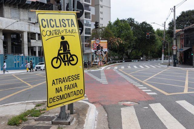 Na rua Sena Madureira, ao fundo, a placa da obra que anuncia o túnel. Em frente, cartaz para ciclistas foi pichado com a frase “contra o túnel”