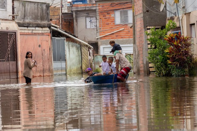 Morador que ajudava família a atravessar a rua alagada, com barco improvisado, se desequilibra e cai na água