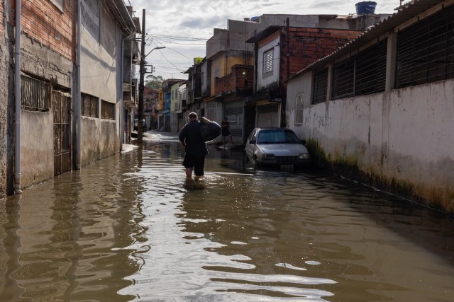 Morador anda por rua completamente alagada no Jardim Pantanal, zona leste de São Paulo (SP)