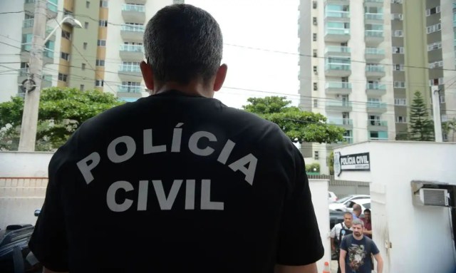 Imagem mostra agente da polícia civil do Rio de Janeiro de costas para a câmera. Ele veste camiseta preta com o nome da polícia civil em branco nas costas