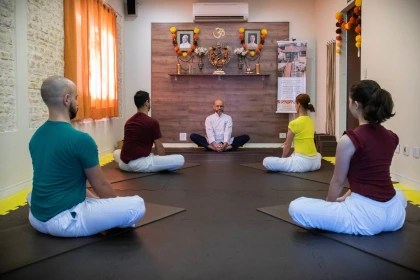Prática de meditação em grupo com instrutor sentado à frente de um altar decorado com símbolos espirituais, conduzida por um guru de ioga
