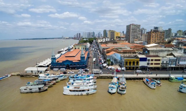 Vista aérea da orla de Belém, com destaque para o Mercado Ver-o-Peso, barcos atracados no porto e prédios do centro da cidade ao fundo.