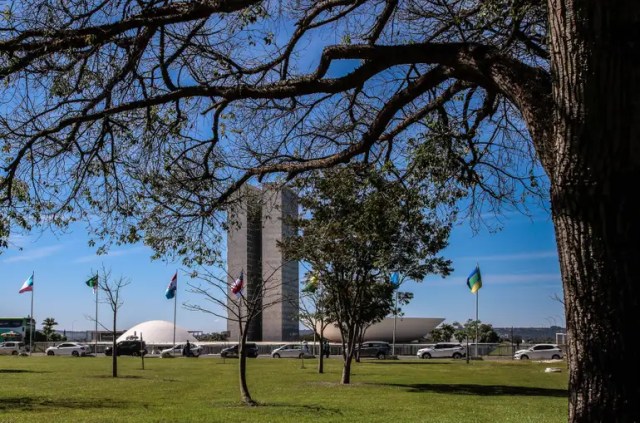 ista do Congresso Nacional em Brasília em dia ensolarado, com árvores em primeiro plano, cenário ligado a Bolsonaro condenado.